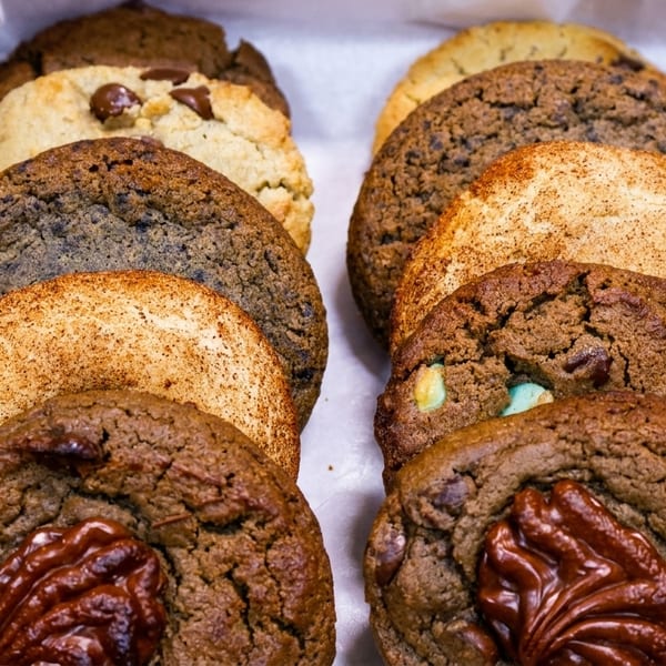 A white box filled with rows of assorted gourmet cookies, including chocolate chip and snickerdoodle.