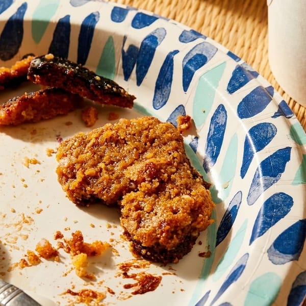 A paper plate with leftover fried chicken, crumbs, and a spoon on a woven placemat.
