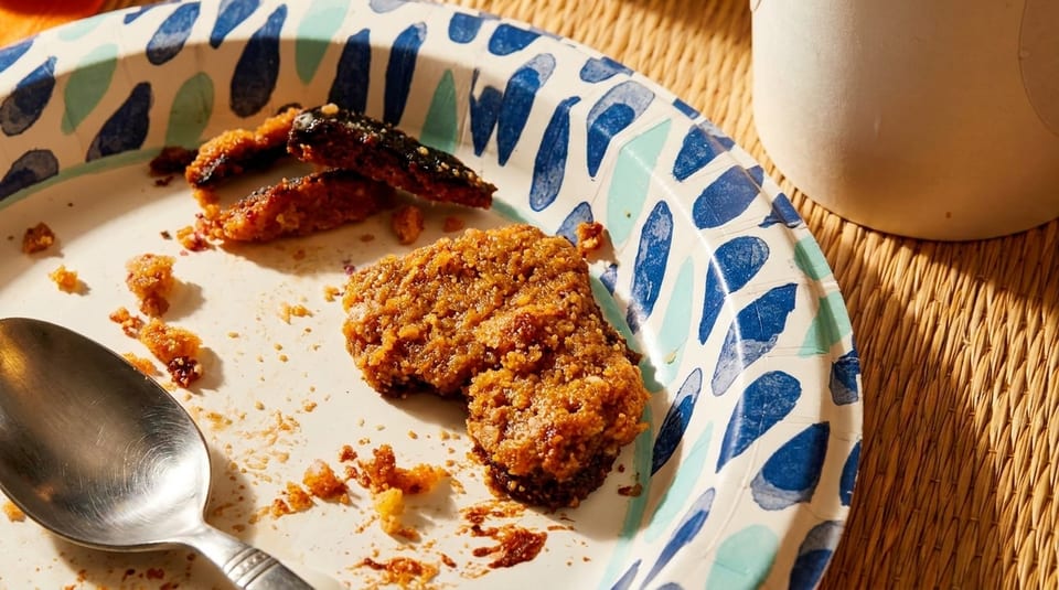 A paper plate with leftover fried chicken, crumbs, and a spoon on a woven placemat.